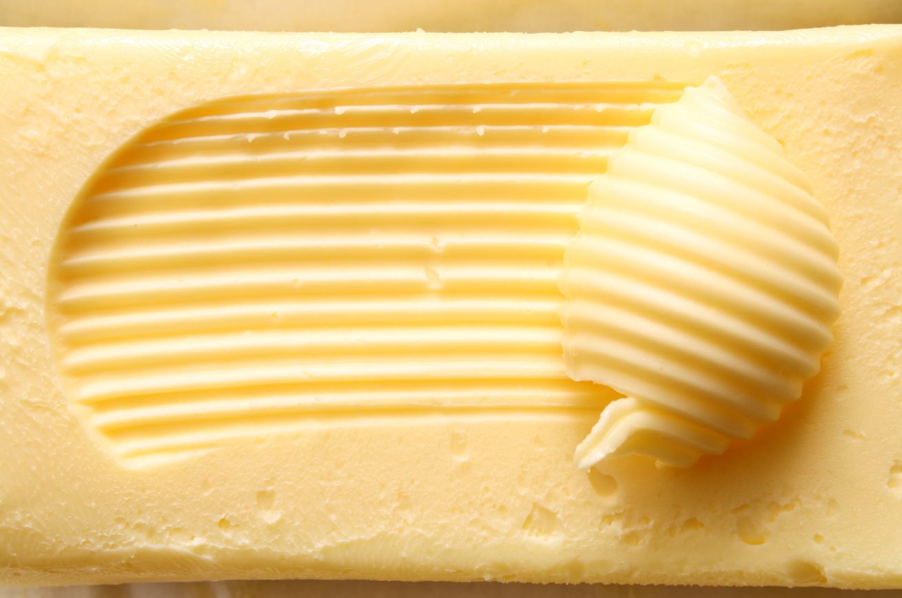 Close up photo of a butter pat with a curl of butter scraped to the right.