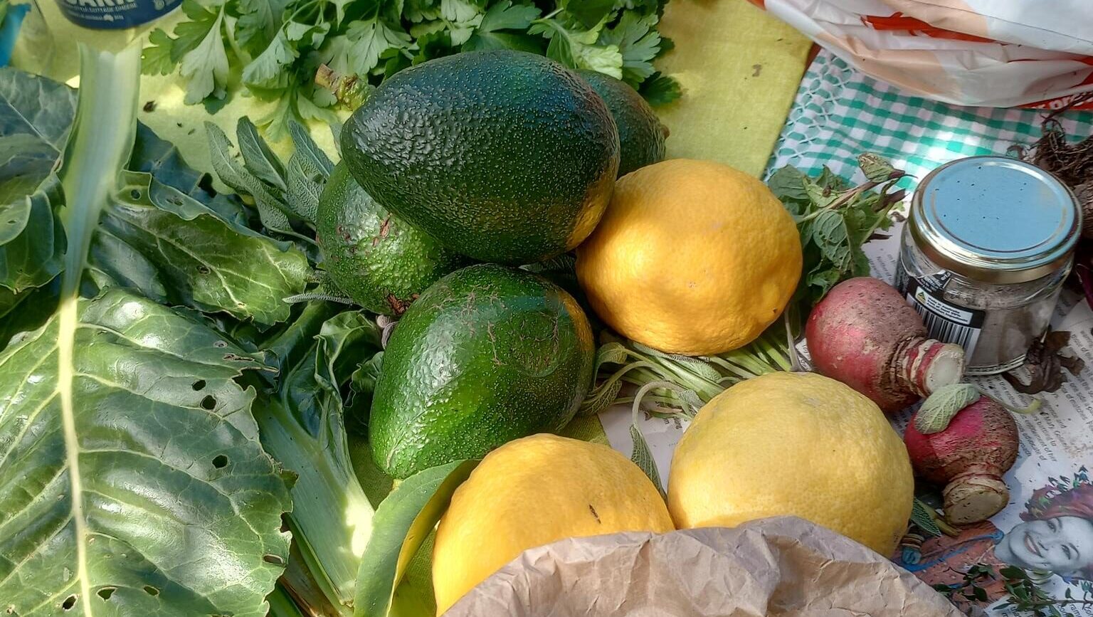 Close up photo of avocados, lemons and leafy green vegetables on a table.