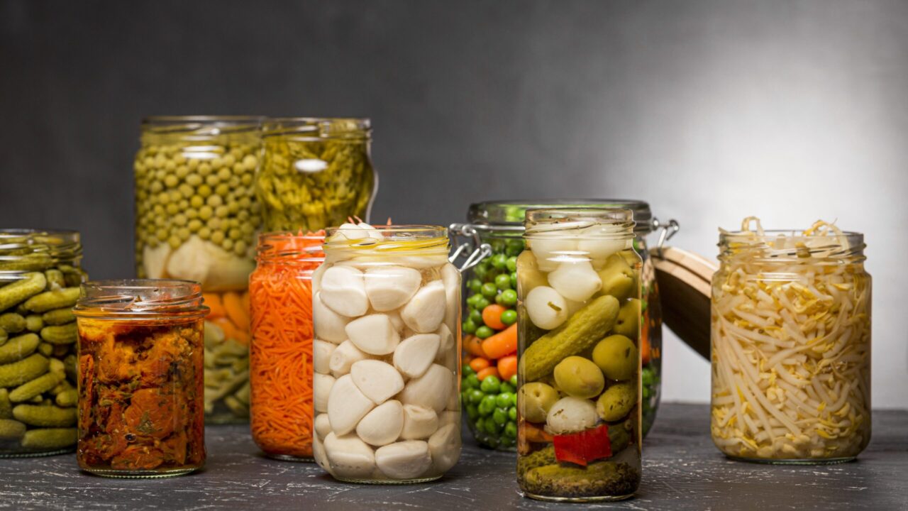 A row of glass jars filled with a variety of pickled vegetables.